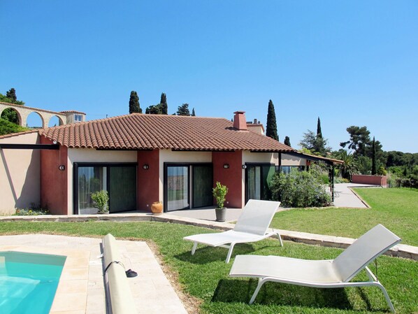Ein modernes Haus mit Swimmingpool, zwei Liegestühlen und einem gepflegten Rasen.