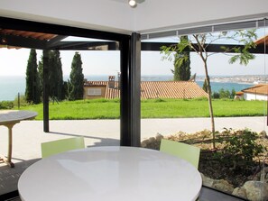Eine moderne Terrassenanlage mit rundem Tisch und Stühlen, mit Blick auf eine Küstenlandschaft mit Häusern und Bäumen.