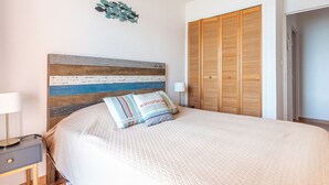Une chambre à coucher comprenant un lit, une table de chevet, une lampe, une tête de lit en bois, une armoire et un élément de décoration murale.