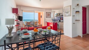 Un coin repas avec vue sur la mer, une cuisine dotée d’un îlot central rouge et un balcon avec des chaises.