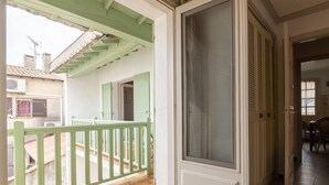 Uma varanda com guarda-corrimão verde, porta de correr de vidro e chão revestido com azulejos.