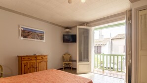Um quarto com cama, cômoda de madeira, cadeira, televisão e varanda com vista para edifícios.