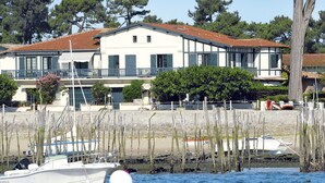 Une propriété située au bord de l’eau, avec un bâtiment blanc, un balcon et un bateau amarré à proximité.