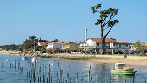 Un paysage côtier avec une rangée de maisons, un phare et un bateau vert sur une eau calme.