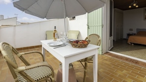 Eine Terrasse mit Tisch, Stühlen, einem Korbwäschesessel und einem gestreiften Sonnenschirm.