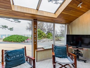 Relax in a spacious room with a high ceiling, skylight, and large windows offering a view of the landscaped outdoor area.