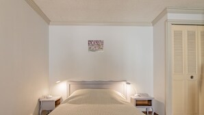 Une chambre à coucher bien rangée, avec un lit, deux tables de chevet dotées de lampes, une porte et un petit élément décoratif mural.