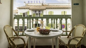 Un balcon avec une table ronde et deux chaises en osier, donnant sur un immeuble sur lequel on peut lire l’inscription « HÔTEL ».