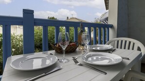 Ein Tisch für zwei Personen mit Tellern, Besteck und Weingläsern auf einem Balkon mit blauer Brüstung.