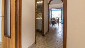 Ein Flur mit Holztür, ein Badezimmer mit gefliestem Duschbereich und ein Essbereich mit Tisch und Stühlen.