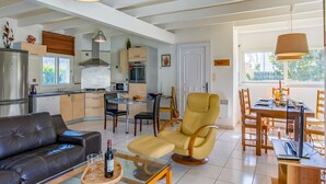 A modern living room with a sofa, a glass coffee table, and a dining area with a table and chairs. - Le Triskell by Interhome (Cléder)