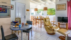 A modern kitchen with a built-in oven, a dining area with a round table and chairs, a comfortable leather armchair, and a television. - Le Triskell by Interhome (Cléder)