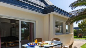 A dining area with a table set for two, a bowl of fruit, and a bottle of orange juice. - Le Triskell by Interhome (Cléder)