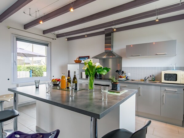 A modern kitchen with a central island, stainless steel appliances, and a large window. - Brise Marine by Interhome (Cléder)