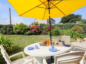 Een ronde buitentafel met blauwe borden en bekers, omringd door witte stoelen, onder een gele parasol.