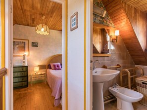 Een slaapkamer met een bed, nachtkastje, lamp en een houten plafond.