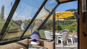 Een zonnedoek met glazen dak, een tafel met stoelen en een gele parasol.