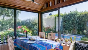 Een terras met een tafel gedekt voor twee personen, omringd door houten stoelen, en uitzicht op een tuin met verschillende planten en bloemen.