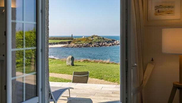 A room with a view of the sea, a stone, and a chair.