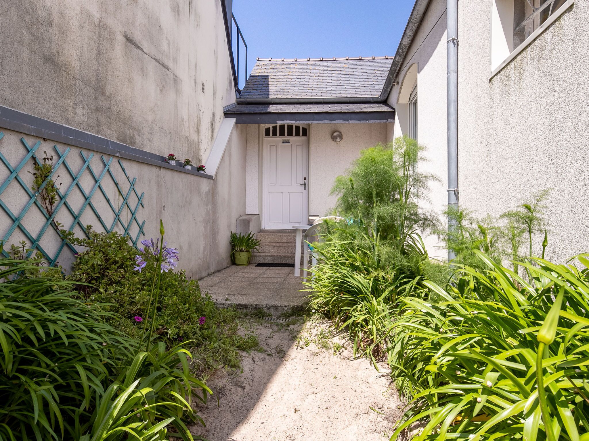 A narrow pathway leading to a white door with a small porch area.