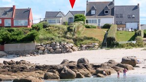 Una propiedad costera con playa rocosa, un muro de piedra y casas con tejados inclinados.