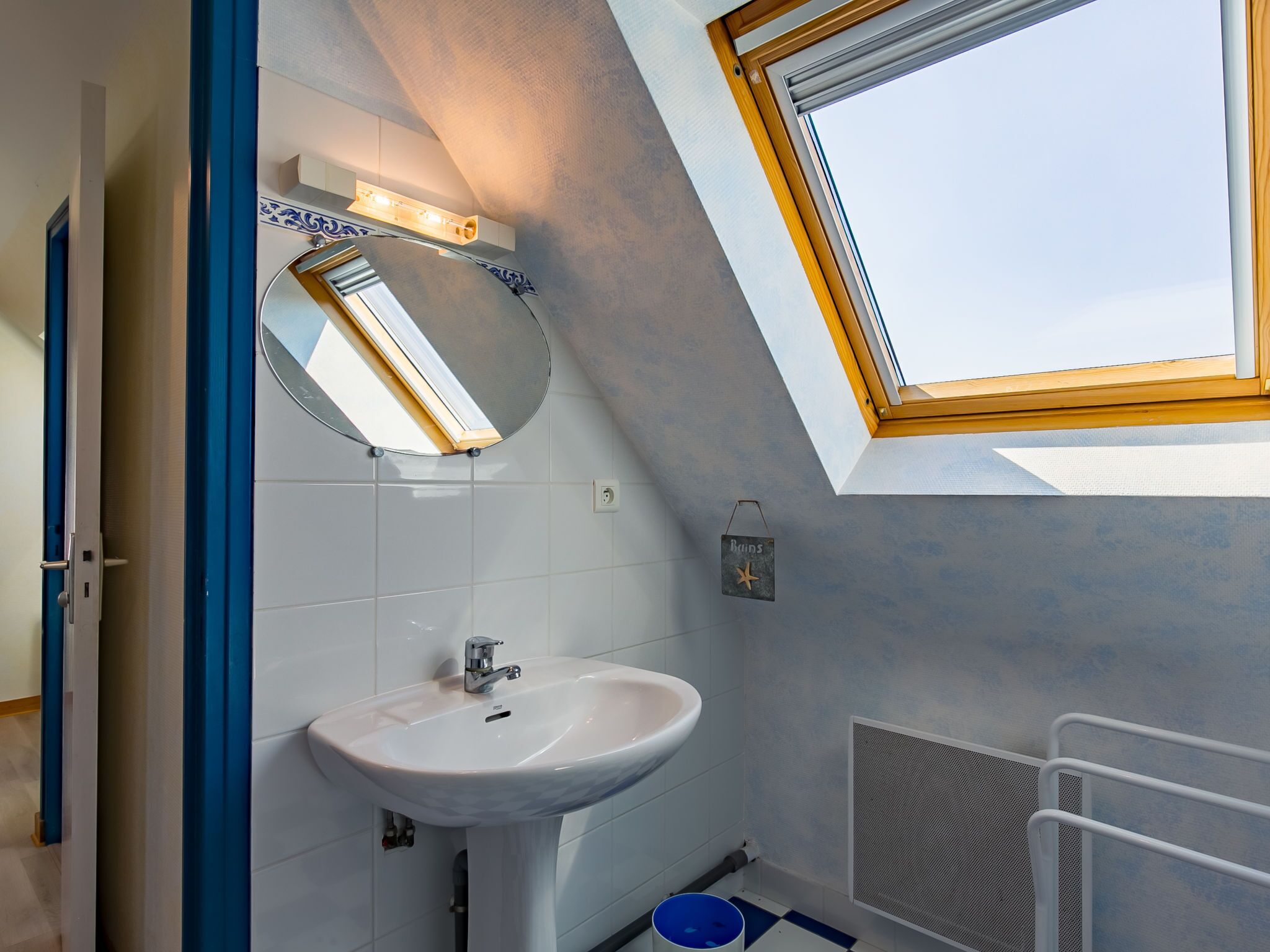 Une salle de bain moderne avec un puits de lumière, un lavabo blanc et un miroir.