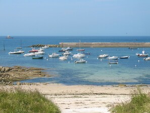 Escena costera con numerosos barcos fondeados en aguas tranquilas, una playa de arena y afloramientos rocosos.