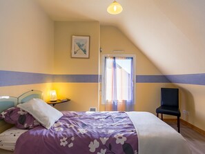Un dormitorio con una cama, una silla, una mesita de noche con lámpara y una ventana con cortinas.