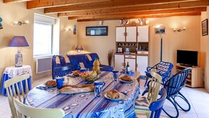 A dining area with a wooden ceiling, a table set with food, chairs, and a television in the background.