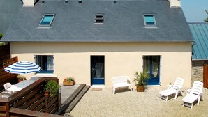 A two-story house with a sloped roof, a balcony, and a small garden area with outdoor furniture.