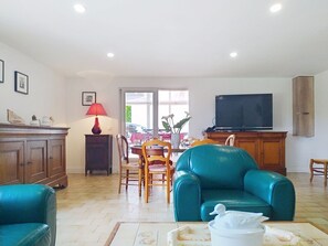 A living room with a teal armchair, wooden dining table, and a television.
