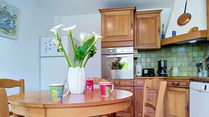 Una cocina con armarios de madera, una mesa de comedor con sillas, un jarrón con flores y una cafetera.