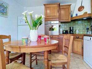 A kitchen with wooden cabinets, a dining table with chairs, a vase with flowers, and a coffee maker.