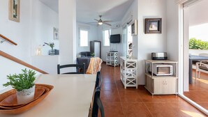 A modern kitchen with white cabinetry, a dining area with a wooden table and chairs, a ceiling fan, and a view through an open door to an outdoor area.