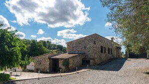 A stone building with a tiled roof, a gravel driveway, and a small patio area with chairs.
