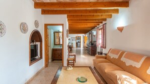 A spacious living room with a wooden ceiling, a sofa, a kitchen in the background, and a dining area.