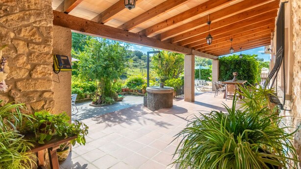 An outdoor patio area with stone walls, wooden beams, and potted plants.