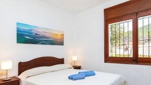 Una camera d'albergo con un letto, due abat-jour, un quadro raffigurante un tramonto sull'oceano e una finestra con sbarre.