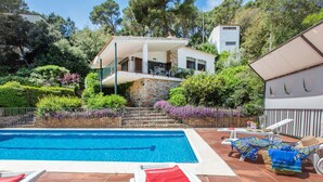 Una piscina con un asciugamano rosso, poltroncine bianche e un edificio in pietra con un balcone sullo sfondo.