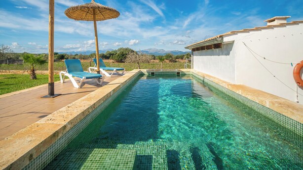 Une piscine à l’eau d’un bleu cristallin, entourée de chaises longues et de parasols, avec en toile de fond des montagnes et un ciel dégagé.