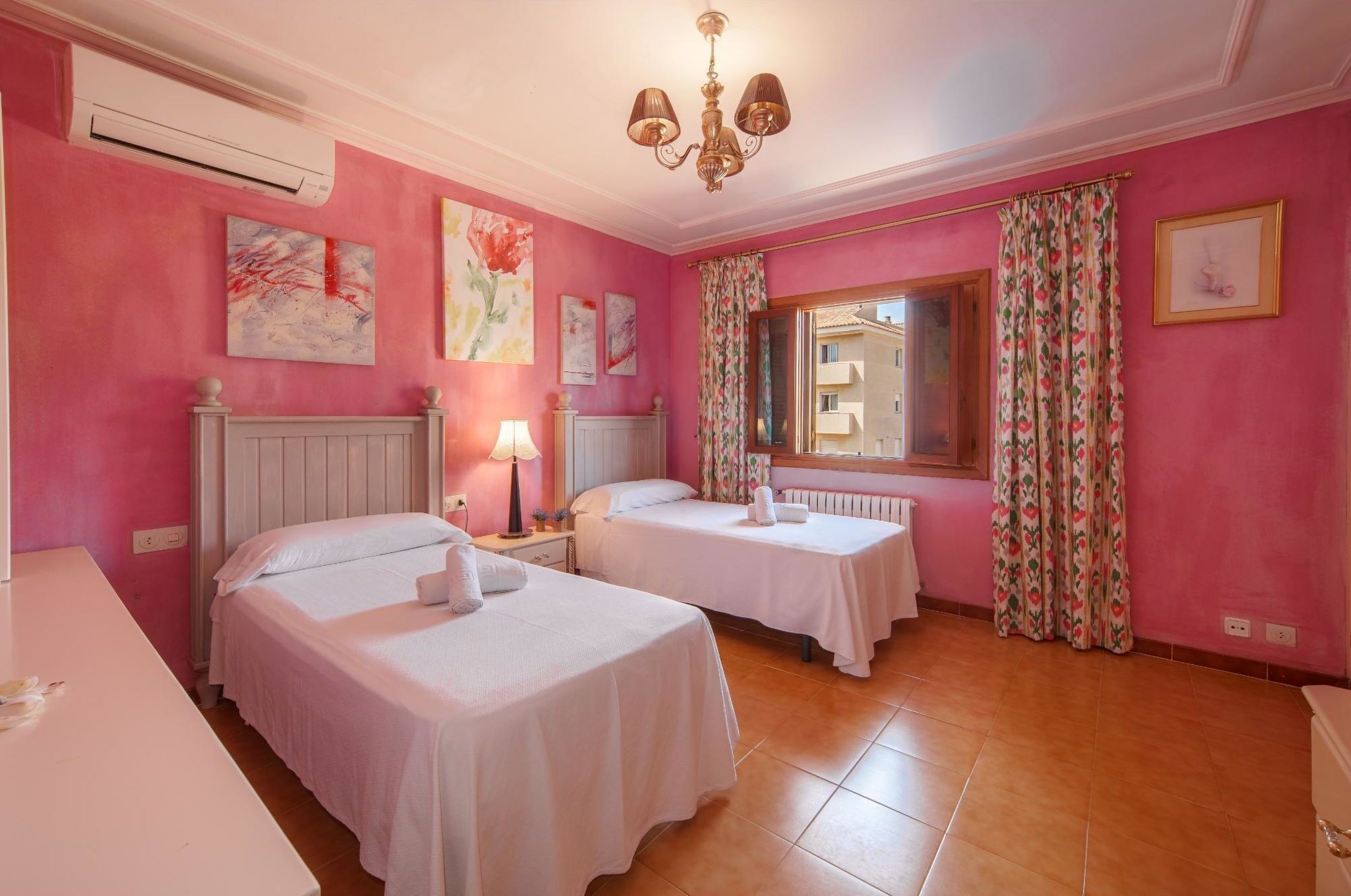 Ein Zimmer mit zwei Betten, einem weißen Schreibtisch, einem Heizkörper, einer Chandelier und rosa Wänden.