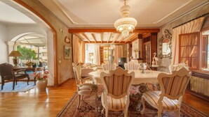 Une salle à manger spacieuse, agrémentée d’un lustre, de poutres en bois et d’une grande fenêtre.