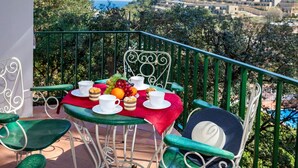 A balcony with a table set for tea, surrounded by greenery and overlooking a scenic view of buildings and trees. - S'Olivera Nº4 by Interhome (Sa Riera)