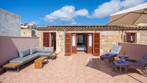 A rooftop terrace with a stone wall, a sofa, a wooden table, and two lounge chairs. - Maria Fumet by Interhome (Capdepera)