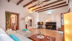 A spacious living room with a sofa, a coffee table, a piano, and a television. - Maria Fumet by Interhome (Capdepera)