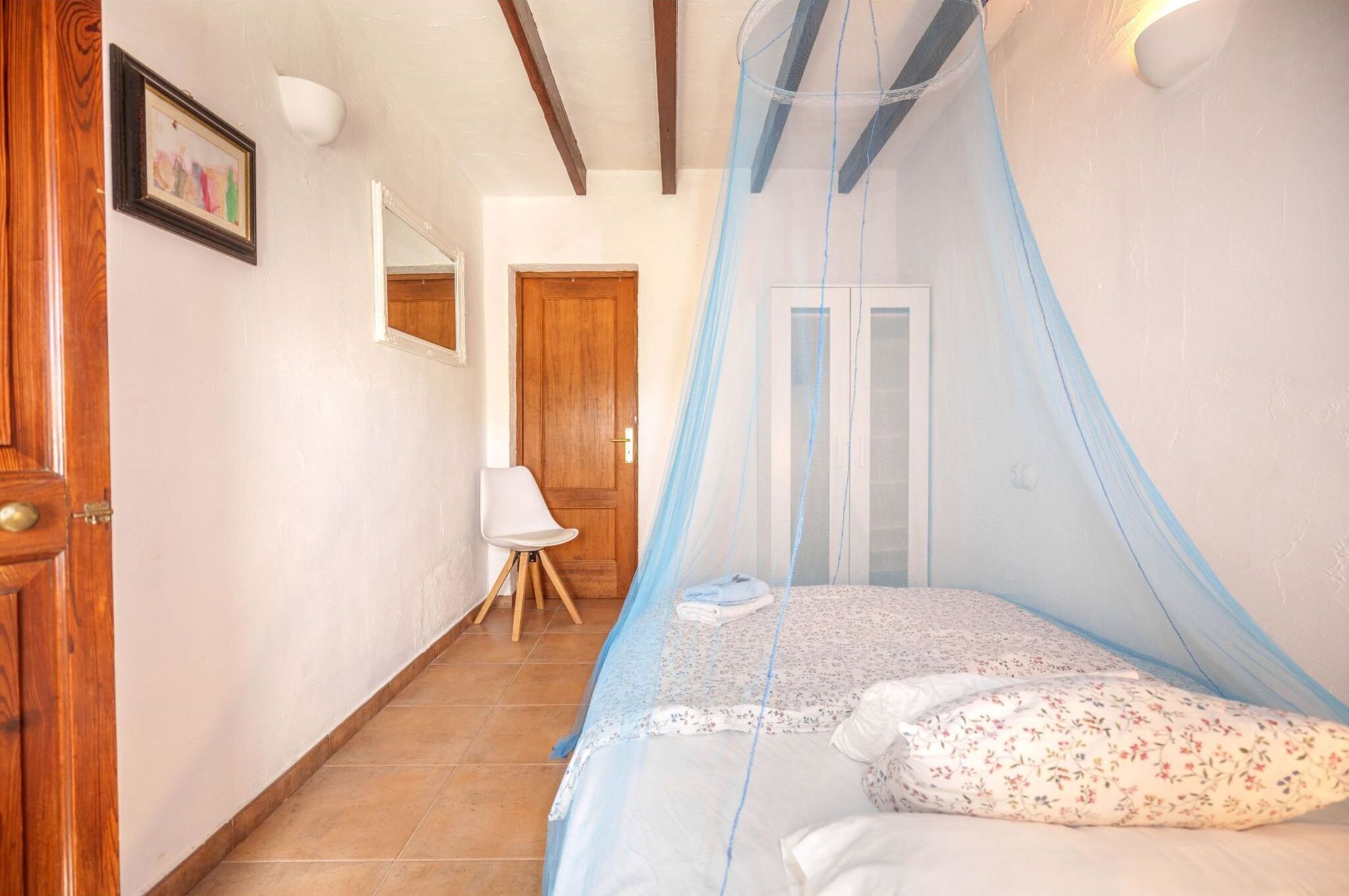 A bedroom with a canopy bed, a wooden door, a white chair, and a framed picture on the wall.