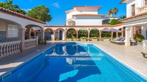 A pool area with a clear blue pool, surrounded by white buildings with arches and tiled roofs.