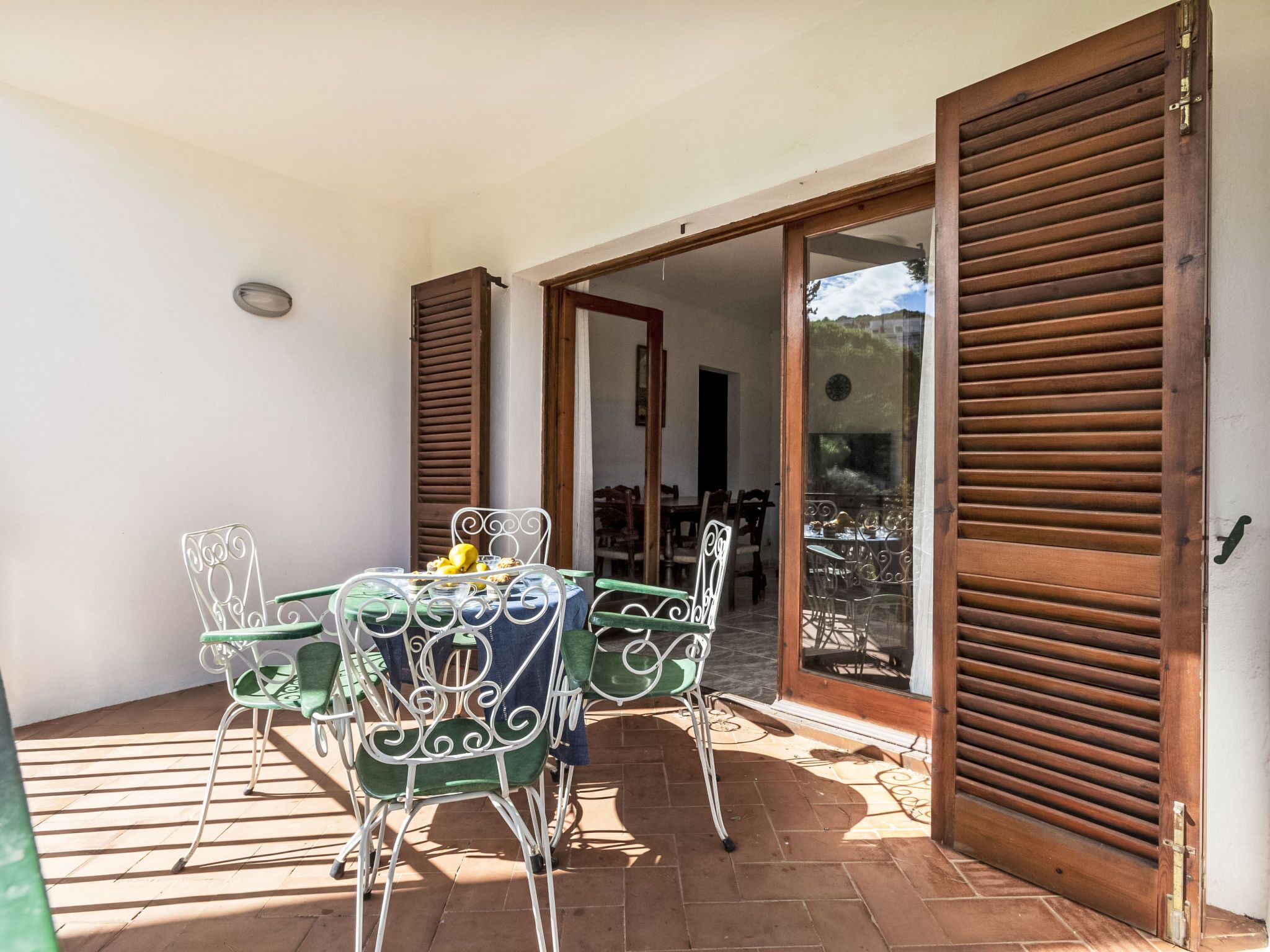 An outdoor patio with a table and chairs, a wooden door, and a view of the interior.