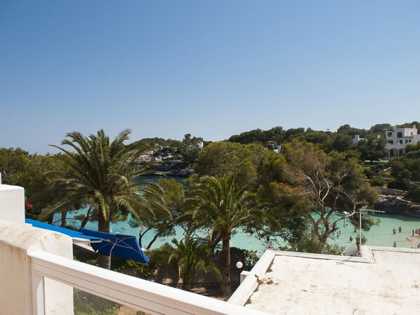 Une vue sur la côte, avec un ciel bleu dégagé, une plage où des gens se baignent, et des bâtiments situés sur une colline en arrière-plan.