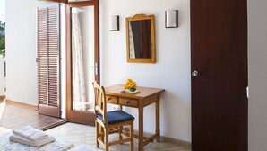 Ein Zimmer mit einem Holztisch, einem Stuhl, einem Bett mit gemustertem Überwurf und einem an der Wand befestigten Spiegel.